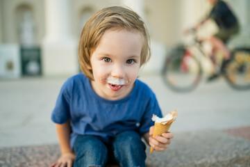 Cute little boy eating tasty fresh ice cream outdoors on warm sunny summer day in Vilnius,...