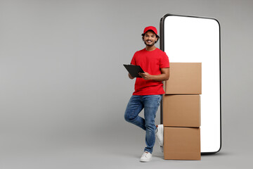 Courier with stack of parcels and clipboard near huge smartphone on grey background. Delivery...