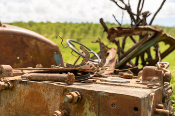 A rusty old tractor is sitting on a rusted old truck. The scene is very old and abandoned