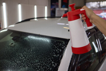 Person spraying car using red and white spray bottle