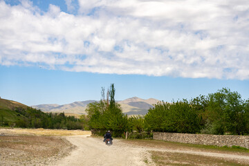 Fototapeta premium A man is riding a motorcycle on a dirt road in the middle of a field. The sky is clear and the sun is shining brightly. The man is wearing a helmet and he is enjoying the ride. The scene is peaceful