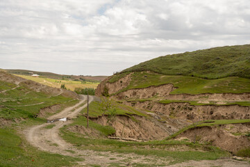 A road cuts through a grassy hillside. The sky is cloudy and the scene is peaceful