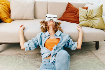 Smiling Woman Enjoying Virtual Reality Game at Home with VR Goggles on Sofa - obrazy, fototapety, plakaty