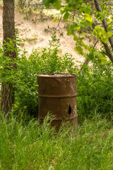 A rusty barrel is sitting in a field of grass. The barrel is old and rusted, and it is surrounded by tall grass. The scene is peaceful and quiet, with the only sounds being the rustling of the grass