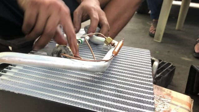 technician is assembling the heat exchanger evaporator component of a car on the street pavement. close up