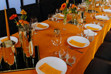 Cutlery, napkins, plates, flowers on an orange table. Table setting. Orange table decor