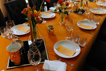 Cutlery, napkins, plates, flowers on an orange table. Table setting. Orange table decor