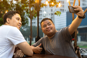 Asian Bestfriends Enjoying Outdoor Cafe, One holding his phone for Taking Selfie or talking in...