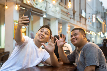 Asian Bestfriends Enjoying Outdoor Cafe, One holding his phone for Taking Selfie or talking in...