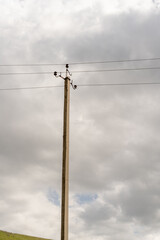 A tall pole with power lines on it. The sky is cloudy and the sun is not visible