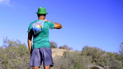 Young adult activist dressed in green with a globe on his shoulders looks at the desert with...