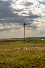 Obraz premium A tall power pole stands in a field with a cloudy sky overhead. The scene is quiet and peaceful, with no people or animals visible
