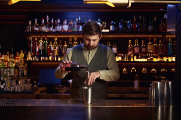 Bartender in uniform pouring drink into shaker behind bar