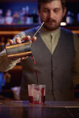 Elegant serious bartender pouring syrup from mix cup into glass