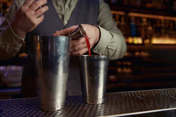 Crop of bartender in uniform pouring drink into shaker behind bar