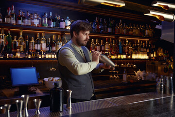 Confident barman mixing cocktail in shaker working in nightclub bar