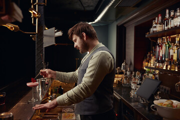 Bartender decorating pink cocktail with rose petal using tweezers