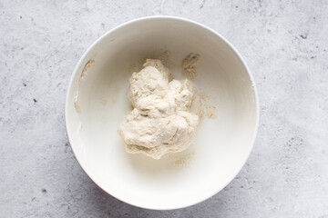 Overhead view of artisan bread dough being mixed in a white mixing bowl, top view of dry low-hydration bread dough