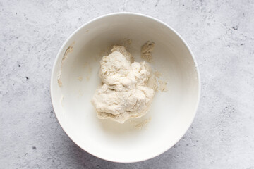 Overhead view of artisan bread dough being mixed in a white mixing bowl, top view of dry...