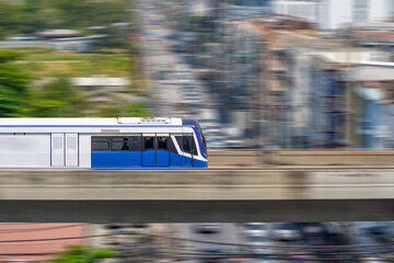 Speed modern commuter train, motion blur rides on a trestle bridge through buildings at height, side view