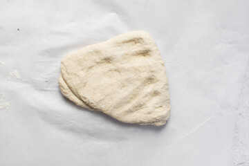  Overhead view of bread dough on parchment lined baking sheet, Shaping proofed dough on a white surface, process of making artisan bread