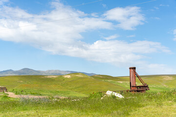 A rusty old structure sits in a grassy field. The sky is clear and blue, with a few clouds...