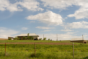 A rural scene with a house and a fence. The sky is cloudy and the grass is green