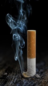 Vertical Smoke of Death Table Butt 4K features a cigarette crushed out on a rustic wooden table top with smoke slowly rising from the tip of the cigarette in a vertical ratio - NOT A.I.
