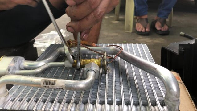 Technician is disassembling the heat exchanger evaporator component of a car on the street pavement. Close up