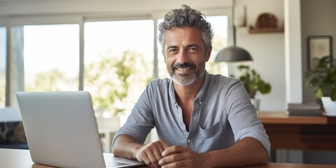 A bearded middle-aged man works at home at a table on a laptop, smiling. happy. Generative AI.