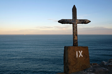 Metal cross in front of the ocean during sunrise