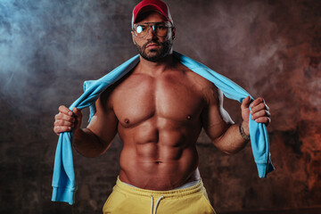 Young strong man bodybuilder in red cap on wall background