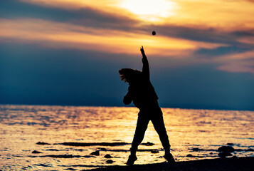 Silhouette of boy throwing stone into the sea at sunset