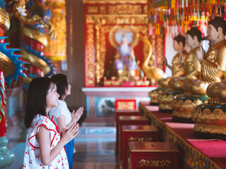 Daughter and mother pay respects to Buddha statue in Chinese shrine