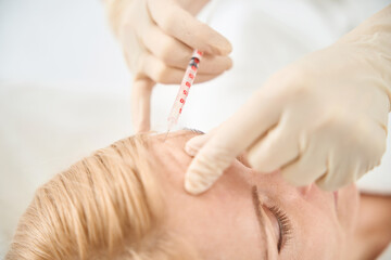 Close-up doctor making microinjections of filler to female client forehead