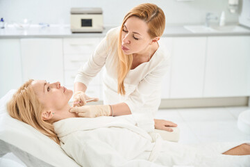 Cosmetologist inserting fillers into female neck to rejuvenate and smooth skin