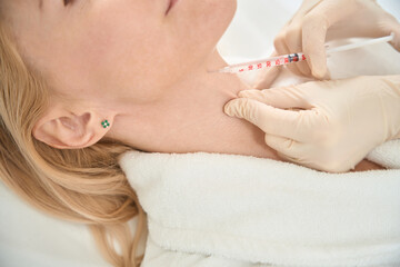 Close-up dermatologist injecting microdose of fillers to female client neck