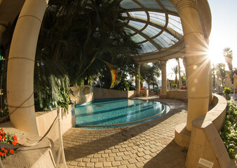 not a deep pool with clear water under a canopy, nearby palm trees and stone columns