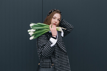 Young woman walking on the street with bouquet bunch of fresh spring tulips flowers, wind cold...