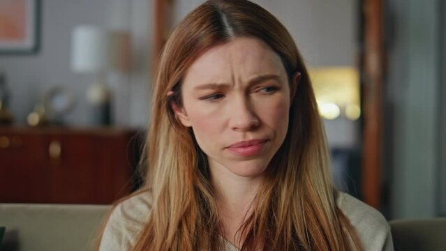 Disappointed woman sitting home couch close up. Portrait dissatisfied young girl