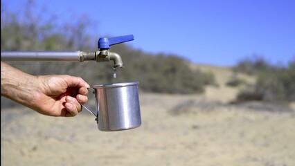 The hand holds the aluminum jug under the dripping faucet in the desert. Lack of water, extreme...