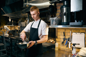 Young caucasian male chef mixing dough with whisk in bowl for cooking dish