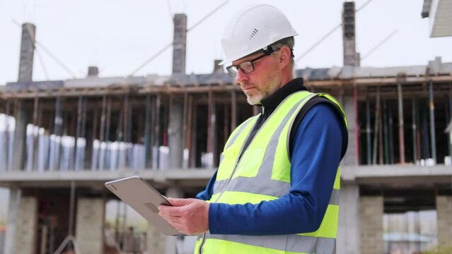 Adult man architect engineer working on buildings site house standing with digital tablet outdoors inspection checklist and blueprints online.