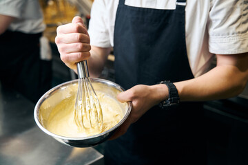 Cropped male chef mixing dough with whisk in bowl for cooking dish in restaurant