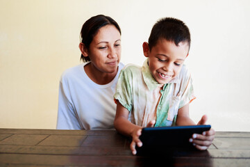 Latin mother and son having fun playing with tablet computer at home. Family relationship and technology concept. Focus on child face