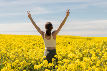 woman arms raised in a yellow field celebrating spring and summer, rear view