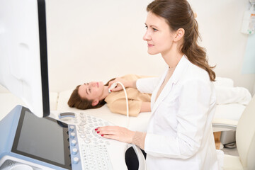 Focused female doctor doing ultrasound scanning of thyroid gland of woman