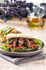 A sandwich with steak, lettuce, and tomato on a grey plate.