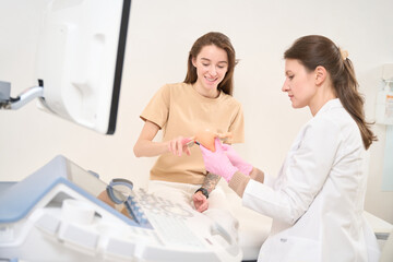 Fototapeta premium Focused female gynecologist showing uterus model to young smiling european woman