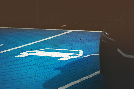 electric car parking and charging bay with parked electric vehicle. blue painted cobblestone and white electric car symbol. sustainable energy concept. selective focus on car symbol. dark surrounding.